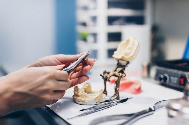 Prótese dentária, mãos femininas trabalhando na dentadura. Foco seletivo.