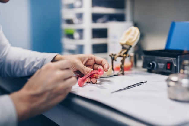 Prótesis dentales, trabajos de prótesis. Cerca de las manos del protésico mientras trabaja en la dentadura. Enfoque selectivo.