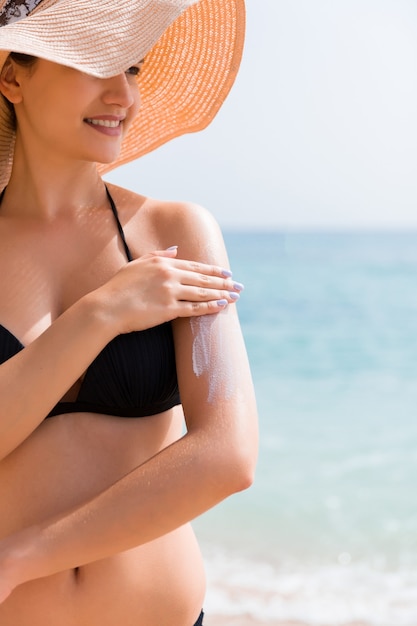 Foto protetor solar de proteção solar. mulher com um chapéu colocando creme solar no ombro ao ar livre sob a luz do sol num lindo dia de verão.