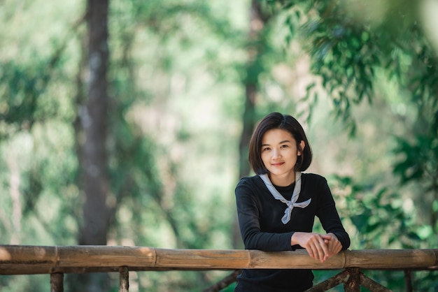 Protrait mujer joven de pie en el puente de bambú sonríe y luce hermosa naturaleza mientras acampa en el bosque con espacio de copia feliz