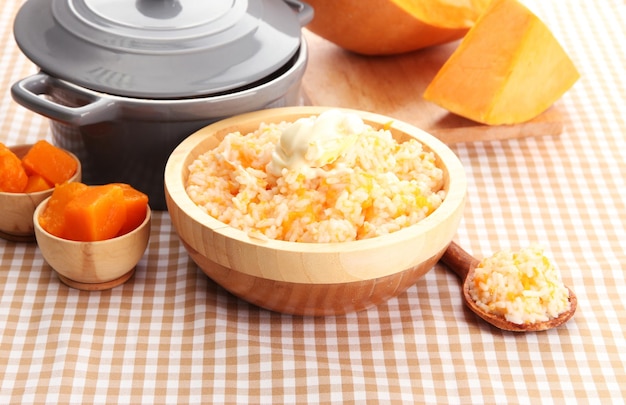 Prove a mingau de arroz com abóbora numa tigela com pano de mesa de fundo