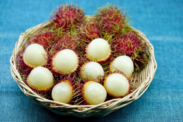 Próximo plano de frutas rambutan maduras em cesta de vime isoladas em toalha de mesa azul