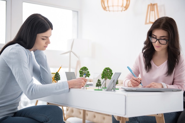 Proyecto ecológico. Mujer inmóvil pensativa y estudiante escribiendo y ayudándose mutuamente con la tarea