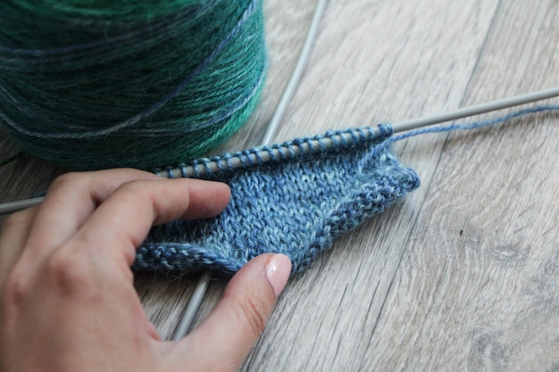 Proyecto de tejido en curso. Hilo azul y agujas en el piso de madera gris. Tejer en la mano de mujer. Hilo seccional multicolor.