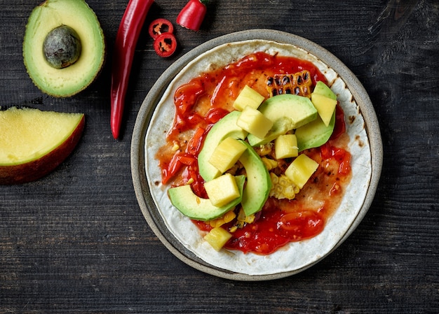 Prozess der Herstellung von mexikanischen Tacos. Teller mit glutenfreier Tortilla und Gemüse auf schwarzem Küchentisch aus Holz, Ansicht von oben