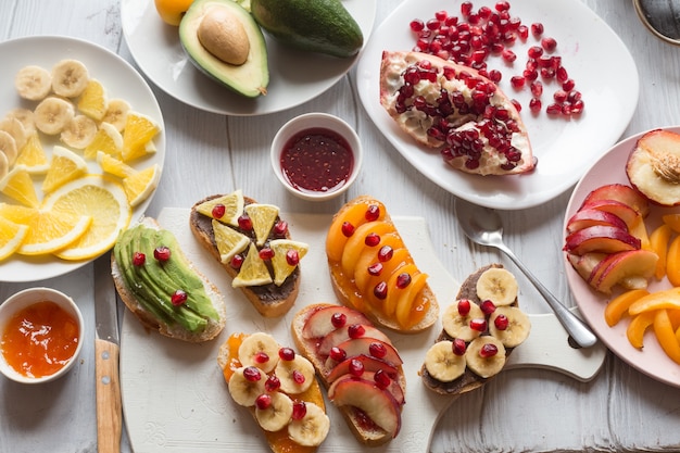 Prozess der Herstellung von süßem Toast mit Marmelade und verschiedenen Früchten Aprikosen, Pfirsichen, Bananen, Orangen und Avocado mit Granatäpfeln dekoriert.