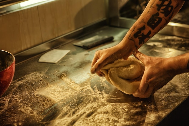 Prozess der Zubereitung und Herstellung von hausgemachten Weißbrothänden mit Tätowierungen von professionellen männlichen Bäckern, die Teig auf dem Tisch mit Mehlkonzept von Kulinarik und Gastronomie herstellen