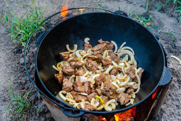 Foto prozess des kochens von köstlichem gebratenem pilaw-fleisch mit zwiebeln in einem kessel im freien