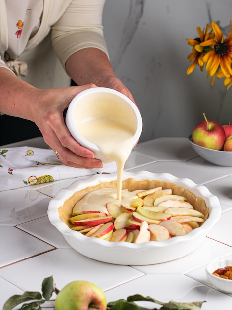 Prozess des Kochens von köstlichem hausgemachtem Apfelkuchen nach Oma-Rezept. Weibliche Hände legen Apfelstücke in Glasbackformen mit Teig. Koch zu Hause Konzept. Charlotte-Kuchen-Form zum Backen ausfüllen.