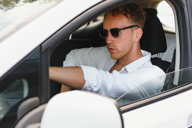 Prueba de conducción de vehículo eléctrico de nueva generación con sistema de conducción autónoma. Hombre caucásico hermoso que se sienta detrás del volante del coche nuevo y moderno y que sonríe a la cámara.