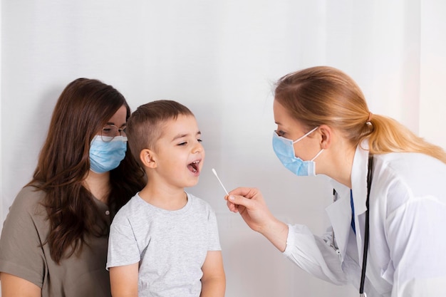 Foto prueba de covid-19 por parte de un pediatra o una enfermera que prueba a un niño pequeño para el coronavirus utilizando el método de hisopo bucal