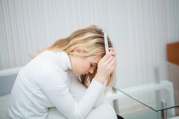 Prueba de embarazo positiva, mujer joven que se siente deprimida y triste después de ver el resultado de la prueba de embarazo en casa