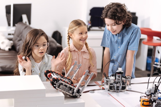 Prueba de juguete robótico. Alumnos encantados sorprendidos inspirados sentados en la escuela y probando juguetes cibernéticos mientras tienen una lección de ciencias