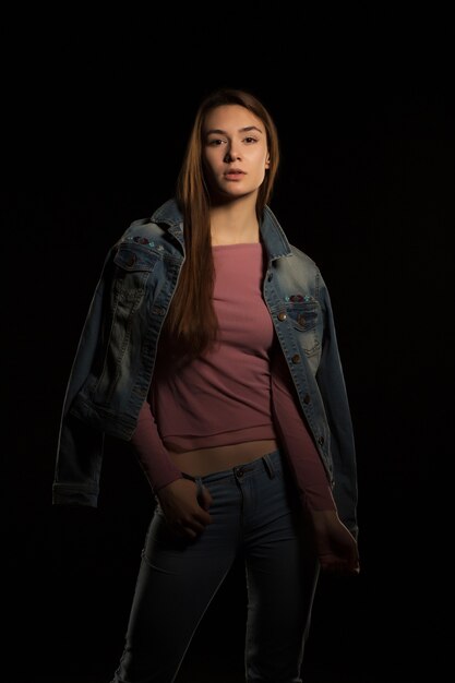 Prueba modelo para mujer bastante segura en chaqueta de jeans posando sobre un fondo negro