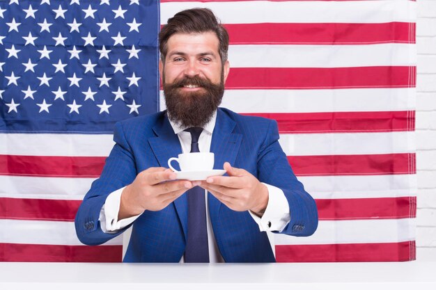 Prueba esto. tomando café en la tribuna. político estadounidense en las elecciones. su campaña electoral. hombre barbudo beber taza de café. Reforma de la educación estadounidense en 4 de julio. Ciudadano estadounidense en la bandera de Estados Unidos.