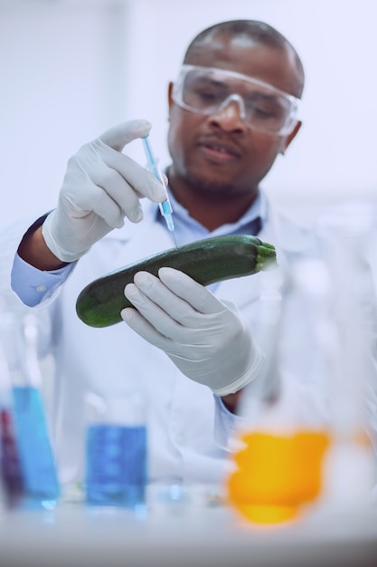 Prueba de vegetales. Biólogo afroamericano concentrado vistiendo un uniforme y probando una calabaza de médula