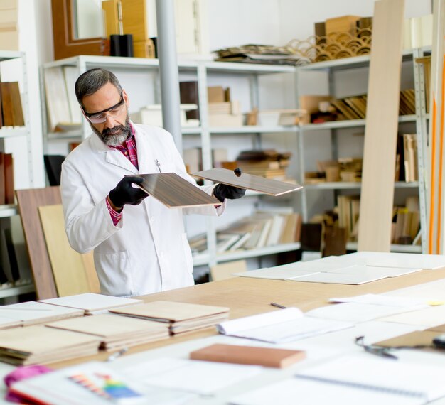 Prüfende Farben des hübschen reifen Ingenieurs auf hölzernen Exemplaren in der Möbelfabrik