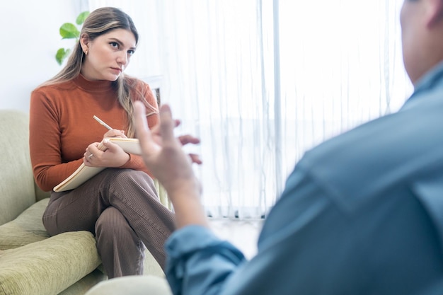 Psicóloga latina olhando atentamente para seu paciente enquanto faz anotações em um caderno