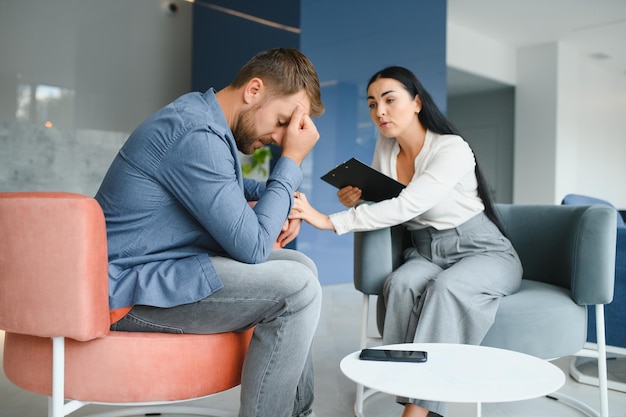 Psicólogo falando com paciente na sessão de terapia Homem deprimido falando com um terapeuta enquanto ela está tomando notas