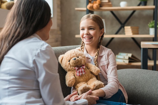 Foto psicólogo feminino, conversa menina, segurando, urso teddy, durante, terapia, sessão