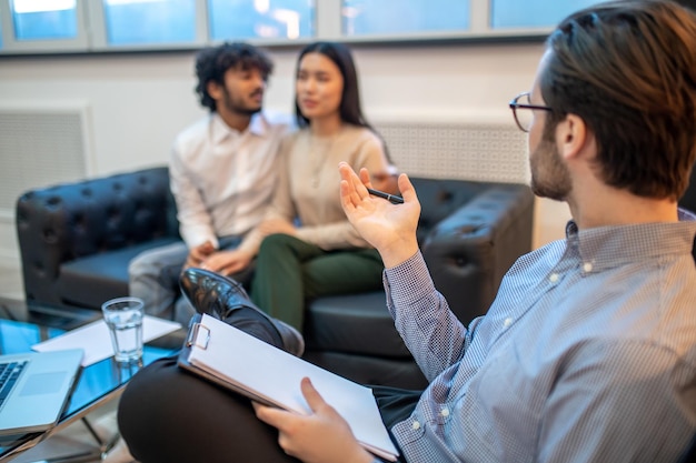 Foto psicólogo profesional hablando con una pareja joven sentada frente a él durante la sesión de terapia de conversación