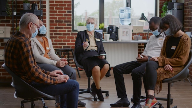 Psicoterapeuta conversando com um grupo de pessoas em uma reunião de terapia sobre recuperação durante a pandemia. terapeuta usando máscara facial, ajudando pacientes de reabilitação com orientação e aconselhamento
