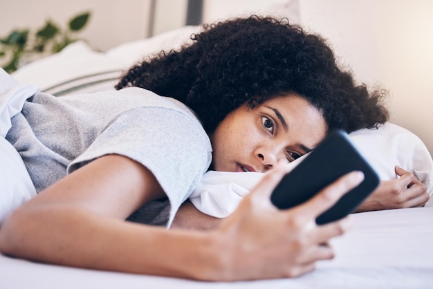 Psychische Gesundheit des Mobiltelefons und Frau in ihrem Bett mit Depressionen, während sie sich Videos in sozialen Medien ansieht Müde, schläfrige und depressive Frau mit Schlaflosigkeit, die sich auf einem Telefon in ihrem Schlafzimmer zu Hause vernetzt