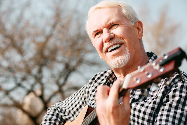 Psychische Gesundheit. Niedriger Winkel des fröhlichen reifen Mannes, der lacht und Gitarrenspiel genießt