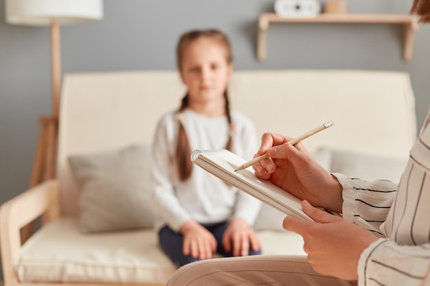 Psychologin macht sich Notizen, während sie eine Sitzung mit einem weiblichen Kind durchführt, indem sie wichtige Punkte über ihren emotionalen und mentalen Zustand aufschreibt und sich die Probleme kleiner Mädchen anhört