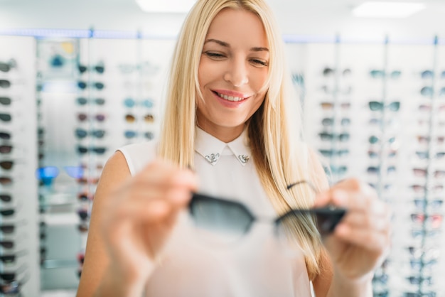 Óptica femenina muestra gafas de sol en la tienda de óptica. Selección de protección ocular con optometrista profesional, concepto de optometría