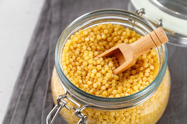 Ptitim Pasta ptitim seca sin cocer en un frasco de vidrio con una cuchara de cuscús israelí