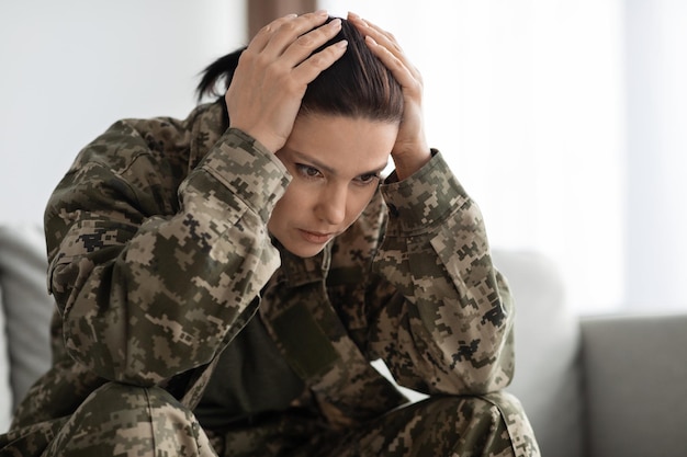 Ptsd y veteranos mujer deprimida en uniforme militar tocando la cabeza con desesperación