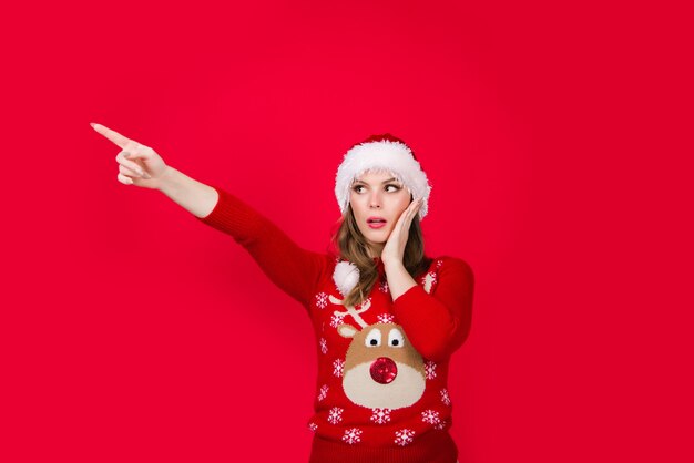 Publicidad de año nuevo. Mujer de Navidad apuntando hacia afuera. Anuncio. Ventas y descuentos. Venta de temporada. Mujer con sombrero de navidad apuntando hacia afuera. Copie el espacio.