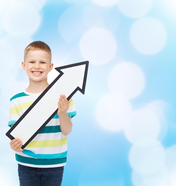 publicidad, dirección y concepto de infancia - niño sonriente con flecha blanca en blanco apuntando hacia arriba sobre fondo azul