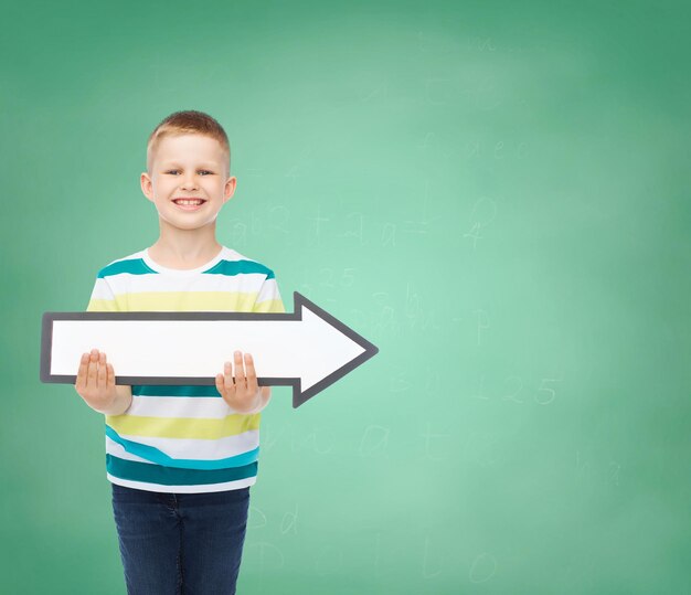 publicidad, dirección, educación y concepto de infancia - niño sonriente con flecha blanca en blanco sobre fondo de tablero verde