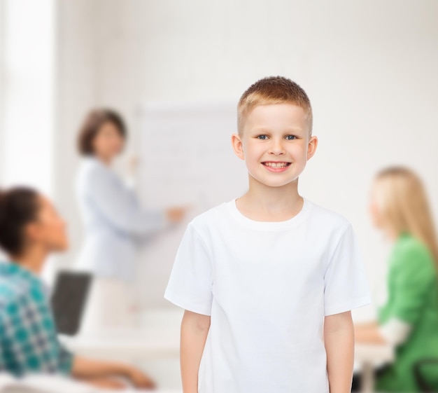 publicidad, escuela, educación, gente y concepto de infancia - niño pequeño sonriente con camiseta blanca sobre un grupo de estudiantes en el aula