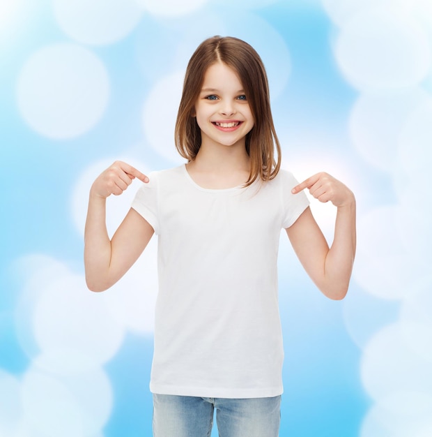 Foto publicidad, gesto, infancia y gente - niña sonriente con camiseta blanca en blanco apuntándose con el dedo sobre fondo azul