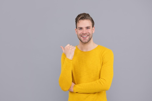 Publicidad. Hombre publicitario. Un tipo feliz señala con el dedo a un lado el fondo gris. Promoción de ventas. Anuncio publicitario. Descuento, copie el espacio.