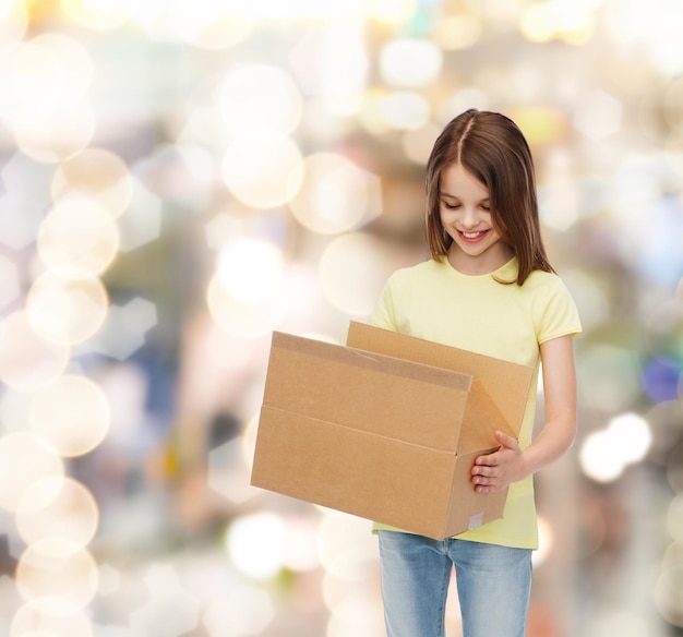 publicidad, infancia, entrega, correo y gente - niña sonriente sosteniendo una caja de cartón abierta y mirándola durante las vacaciones