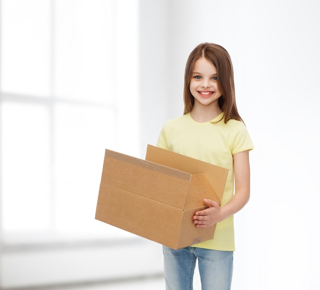 publicidad, infancia, entrega, correo y gente - niña sonriente sosteniendo una caja de cartón abierta sobre el fondo de la habitación blanca