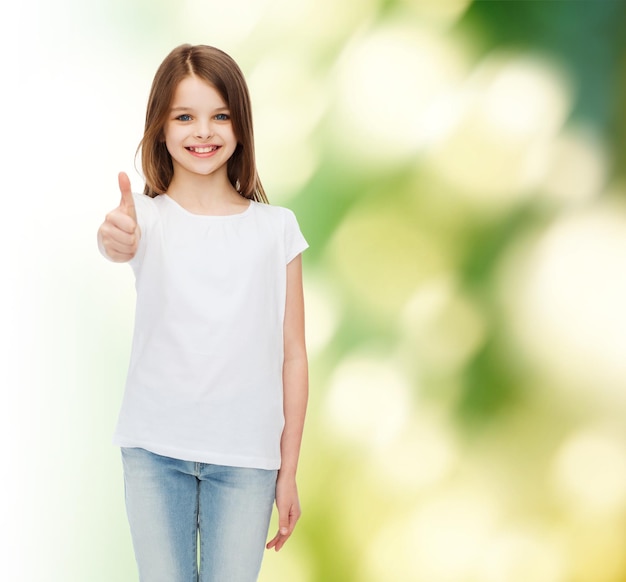 publicidad, niñez, ecología y gente - niñita sonriente con camiseta blanca mostrando pulgares arriba gesto sobre fondo verde