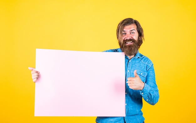 Foto publicidad de su producto. emociones humanas. chico sin afeitar con pelo largo peinado. peluquería y peluquería. belleza y moda masculina. feliz hombre barbudo. brutal hipster caucásico mantenga papel, copie el espacio.