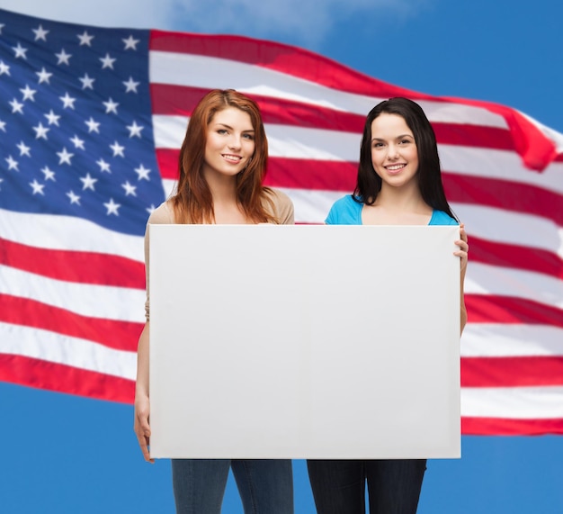 Foto publicidad, venta y concepto de la gente - chicas jóvenes sonrientes con una pizarra en blanco sobre el fondo de la bandera americana