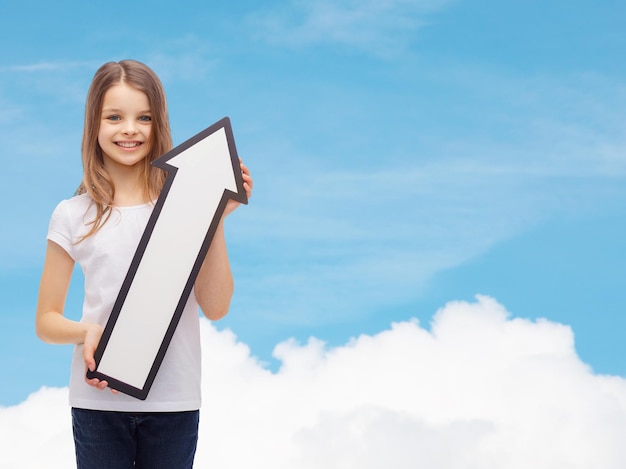 Publicidade, direção, ar, aviação e conceito de infância - menina sorridente com seta branca em branco apontando para cima sobre o fundo do céu azul