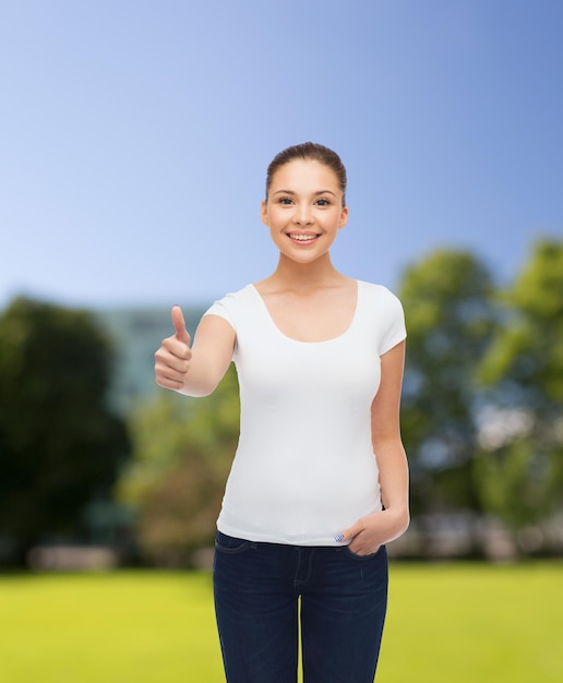 publicidade, férias de verão, gesto e conceito de pessoas - jovem sorridente em camiseta branca em branco, mostrando os polegares sobre o fundo do parque