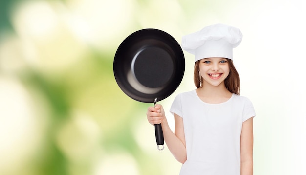 publicidade, infância, culinária e pessoas - garota sorridente em camiseta branca e chapéu de cozinha segurando a panela sobre fundo verde