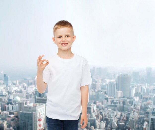 publicidade, pessoas e conceito de infância - menino sorridente em camiseta branca em branco sobre o fundo da cidade