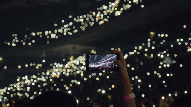 Publikum mit Lichtern im Konzertsaal und Frau, die mobiles Video aufnimmt