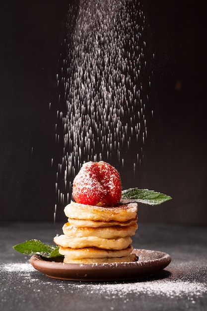 Puderzucker bestreut winzige Pfannkuchenflocken mit Erdbeeren, Minze und Honig