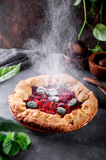 Puderzucker wird auf hausgemachten Kuchen mit Erdbeeren auf dem Tisch Sommergebäck mit gegossen